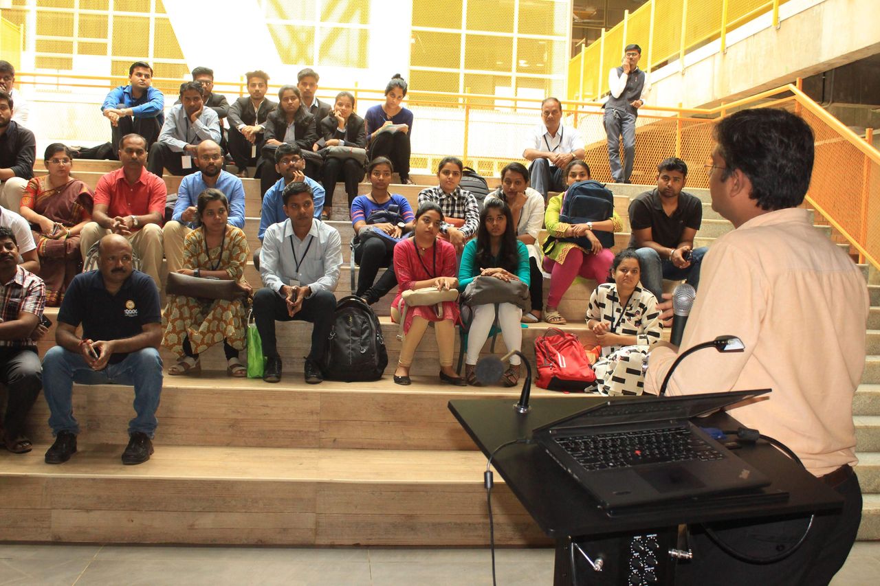 A speaker at a lectern addressing a seated audience on tiered steps