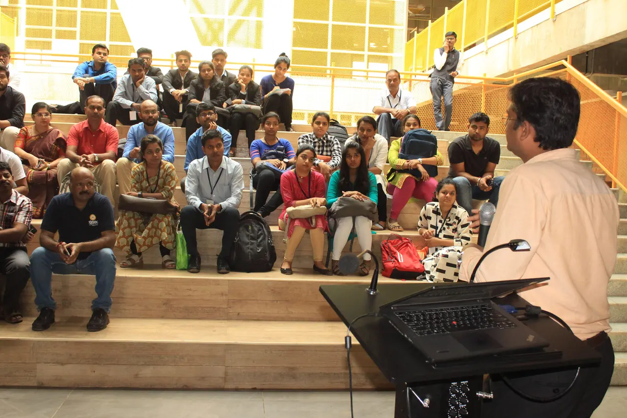 A speaker at a lectern addressing a seated audience on tiered steps