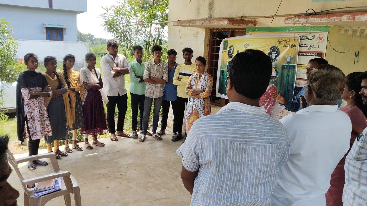 Students gathered outdoors at a rural centre, listening to a talk during a field visit
